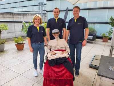 Drei Mitarbeiter stehen neben einem Mann im Rollstuhl auf einer Terrasse.