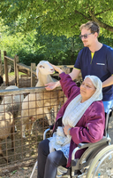Eine Frau im Rollstuhl streichelt ein Schaf, während ein Mann sie unterstützt.