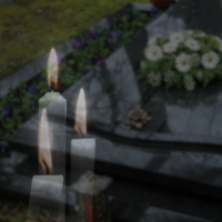 Drei brennende Kerzen vor einer Grabstätte mit Blumen.