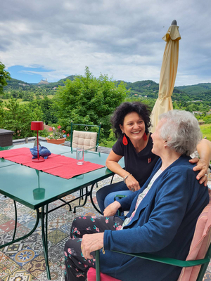 Zwei Frauen sitzen gemütlich an einem Tisch im Freien und unterhalten sich.