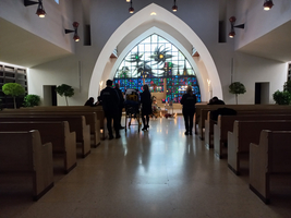 Menschen stehen in einer Kirche vor einem bunten Fenster und Bänken.
