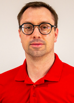 Ein Mann mit Brille trägt ein rotes Polohemd und schaut in die Kamera.