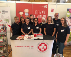 Gruppe von Ehrenamtlichen auf Messe hinter Pult mit Samariterbund Wien Logo